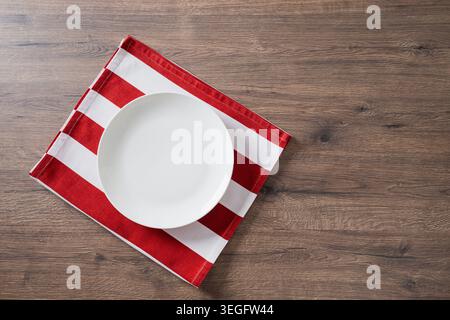 Leerer weißer Teller auf rot gestreifter Serviette über Holztisch Stockfoto