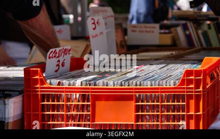 In der Orangenkiste befinden sich verschiedene Musik-CDs auf einem Markt im Freien, mit Preisschildern und einem verschwommenen Hintergrund von Büchern und Leuten, die in der Nähe stöbern Stockfoto