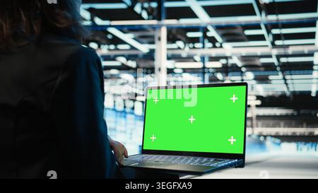 Green-Screen-Laptop, der vom Programmierer im Rechenzentrum zur Fehlerbehebung bei Elektronikproblemen verwendet wird. IT-Profis im Serverraum verwenden ein Modell-Notebook zur Analyse von Systemprotokollen, Reparieren von Gerätestörungen bei Kamera A Stockfoto