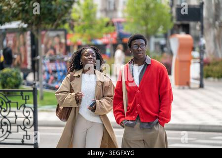 Glückliche, sorglose afroamerikanische Männer und Frauen, die sich unterhalten und lächeln, wenn sie die Straße hinunter laufen. Stockfoto