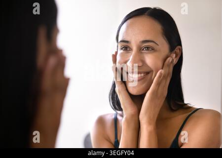 Lächelnde Frau, die das Gesicht nach Hautpflegeprogramm berührt Stockfoto