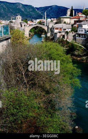 Stari überspannt den Neretva River in Mostar, B&H, umgeben von alten Steinhäusern und majestätischen Bergen. Stockfoto