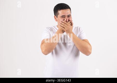 Verblüffter junger Mann, der den Mund schließt und beide Hände geschockt hat Stockfoto