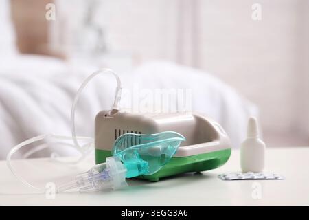 Moderner Vernebler mit Nasentropfen und Pillen auf dem Tisch im Schlafzimmer Stockfoto