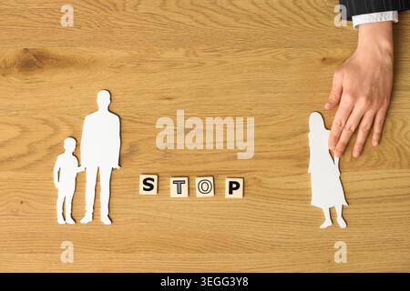 Weibliche Mediatorenhand mit Familienfigur und WORTSTOPP auf Holztisch, Blick von oben Stockfoto