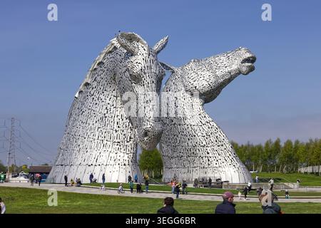 Besucher versammelten sich unter den Kelpies im Helix Park in Falkirk, Schottland, unter einem blauen Himmel mit verstreuten Wolken. Stockfoto