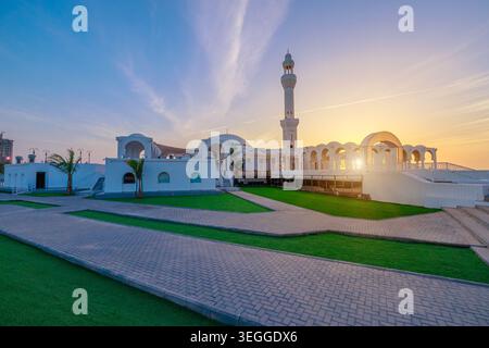 Al Rahmah Moschee am Roten Meer in Dschiddah, Saudi-Arabien, mit dem JYC Jeddah Yacht Club Gebäude, das eine malerische Szene bei Nacht schafft Stockfoto