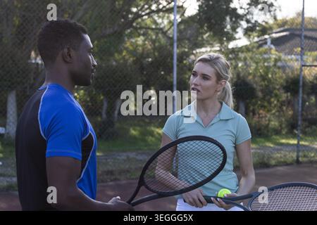 Verschiedene Tennispartner üben auf dem roten Platz in Sportbekleidung, halten Schläger und Tennisball Stockfoto
