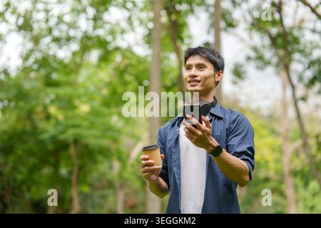 Asiatischer Mann mit Smartphone und Kaffeetasse im Park Stockfoto