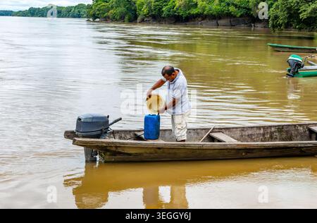 Raudal del Guayabero, Guaviare, Kolumbien - 1. Mai 2026 - ein ortskundiger Reiseleiter gießt Wasser aus einem gelben Eimer in einen blauen Behälter, während er auf einem hölzernen Kanu fährt. Stockfoto