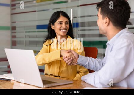 Lächelnde südasiatische Geschäftsfrau, die sich mit einem männlichen Kollegen die Hand schüttelt Stockfoto
