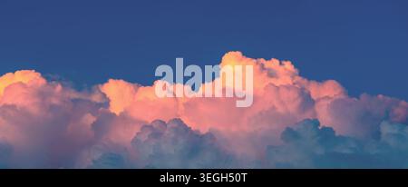 Lebendiges Gemälde bei Sonnenuntergang mit Kumuluswolken, die in Gold- und Rosa-Tönen vor einem tiefblauen Himmel beleuchtet sind, schaffen ein atemberaubendes und friedliches A Stockfoto