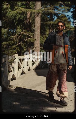 Ein stilvoller junger Mann, der über eine rustikale Holzbrücke in den Bergen von Chakrata, Uttarakhand, Indien, spaziert. Stockfoto