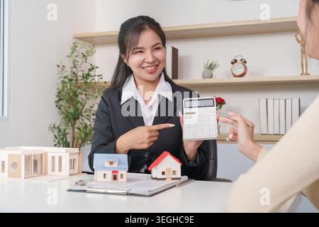 Asiatische Immobilienmaklerin zeigt dem Kunden im Büro einen Rechner Stockfoto