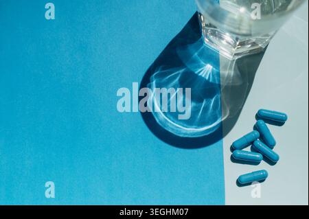 Draufsicht auf Arzneimittelpillen und ein Glas Süßwasser auf blauem Hintergrund. Hydratationskonzept bei Medikation, klinischer Verordnung und o Stockfoto