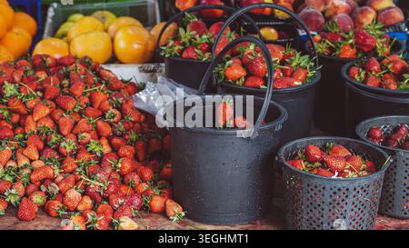 Frische Erdbeeren, verpackt in schwarzen Plastikeimern und Körben an einem Marktstand Stockfoto