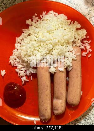 Einfache hausgemachte Mahlzeit mit gekochtem weißem Reis, Würstchen und Ketchup auf einem hellen Teller. Preisgünstiges Essen für jeden Tag und schnelles Mittagessen oder Abendessen. Stockfoto