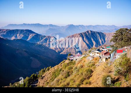 Ein malerischer Blick auf eine abgelegene Bergsiedlung auf einem steilen Hügel mit mehrschichtigen Berggipfeln im Hintergrund in Chakrata, Uttarakhand, Indi Stockfoto