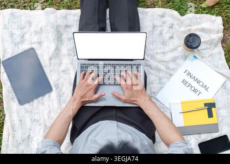 Asiatischer Mann, der auf einem Laptop den Finanzbericht überprüft, während er im Park arbeitet Stockfoto