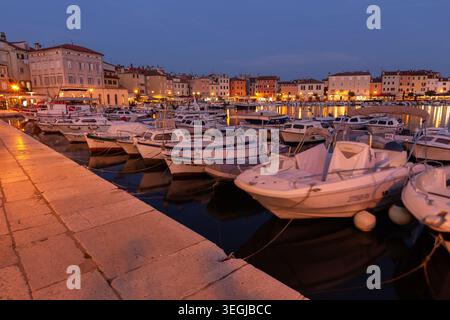 Kleine Boote legten in der Abenddämmerung an der Marina im Hafen von Rovinj mit farbenfrohen Altstadtgebäuden in Istra, Kroatien, an. Stockfoto