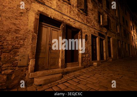 Stein- und Backsteinfassade mit alten Holztüren auf einer Kopfsteinpflasterstraße in der Altstadt von Rovinj, Kroatien bei Nacht. Stockfoto