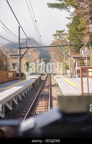 Eine friedliche Reise durch Hakone, Japan, mit dem historischen orangen Bergzug, der steile Strecken fährt und Seilbahnen in dicken Zügen verschwindet Stockfoto