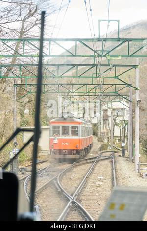Eine friedliche Reise durch Hakone, Japan, mit dem historischen orangen Bergzug, der steile Strecken fährt und Seilbahnen in dicken Zügen verschwindet Stockfoto