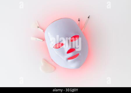 Trendige Hautpflege-Komposition mit futuristischer LED-Gesichtsmaske und Beauty-Accessoires auf weißem Hintergrund. Luxuriöse Hautpflege und Beauty-Konzept. Stockfoto