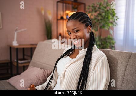 Junge Afroamerikanerin lächelt zu Hause auf dem Sofa Stockfoto