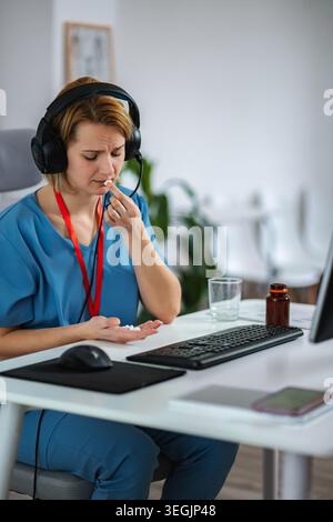 Gestresster medizinischer Mitarbeiter, der am Schreibtisch Pillen mit Headset nimmt Stockfoto