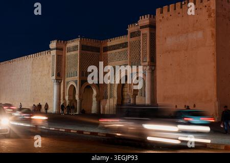 Das Bab Mansour-Tor ist bei Nacht beleuchtet und zeigt die komplizierte islamische Architektur und fängt die Verkehrsbewegung in Meknes ein Stockfoto