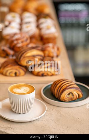 Eine minimalistische Coffee-Shop-Tischszene mit einem heißen Cappuccino und einer frischen Schokolade Pain au Chocolat auf einer grünen Platte, mit einer Hintergrundanzeige von Stockfoto