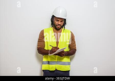 Ein Bauarbeiter in reflektierender Weste und Schutzhelm macht Notizen auf weißem Hintergrund. Stockfoto