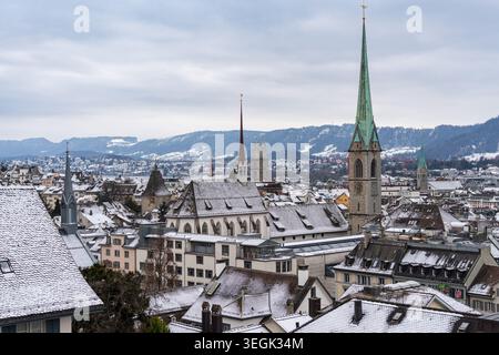 Winterblick auf die verschneiten Dächer in Zürich von der Polyterrasse mit dem Fraumunster Turm und den Bergen in der Ferne Stockfoto