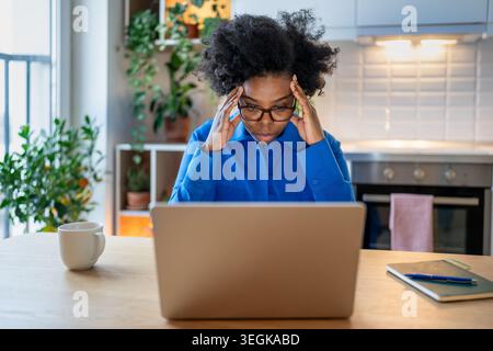 Die erschöpfte schwarze Frau, die sich nicht mehr konzentrieren kann, arbeitet von zu Hause aus auf dem Laptop und fühlt sich abgelenkt. Stockfoto