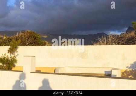 Lange Abendschatten auf einer weißen Wand unter dramatischen Wolken in Agaete, Gran Canaria, den Kanarischen Inseln, Spanien. Minimalistisches Reisefoto mit warm Stockfoto