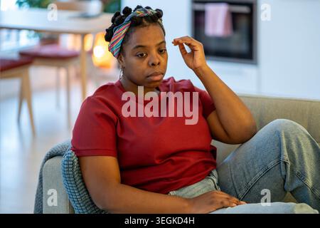 Schwierige Lebensphase einer traurigen schwarzen Frau, die nachdenklich auf dem Sofa sitzt, überfordert von Sorgen, Angst. Stockfoto