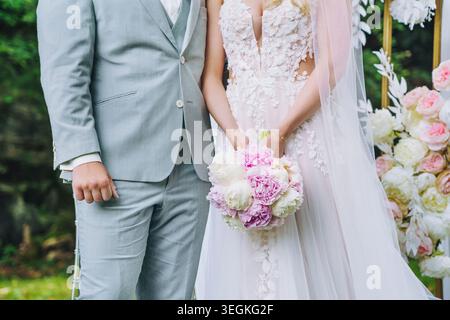 Glückliche, lachende Braut und Bräutigam auf der Hochzeit auf der offenen Hochzeit. Nahaufnahme der Hände mit Hochzeitsstrauß. Stockfoto