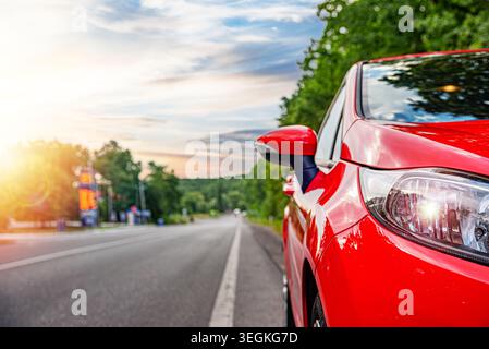 Ein pulsierendes rotes Auto parkt am Rande einer leeren Asphaltstraße, umgeben von grünen Bäumen Stockfoto
