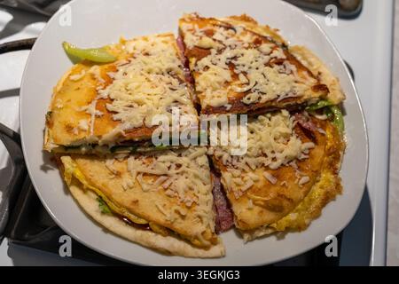 Ein Hochwinkelfoto einer hausgemachten Frühstücktortilla, die auf einer weißen Keramikplatte in vier Viertel geschnitten wurde. Das goldbraune knusprige Flatbr Stockfoto