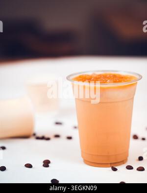 Eiskaffee in einer Plastiktasse mit gerösteten Kaffeebohnen und Pappbechern auf einer weißen Oberfläche Stockfoto
