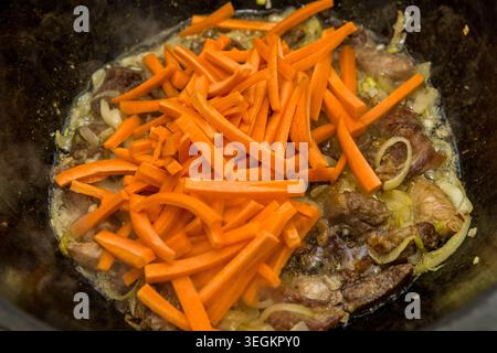 Frische Karottenstäbchen zu Lammfleisch und Zwiebeln in traditionellem kasan für usbekische Plov-Küche, authentische asiatische hausgemachte Küche. Stockfoto