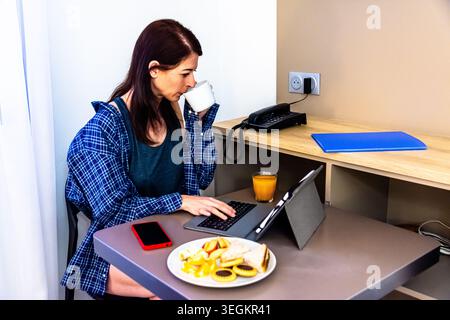 Frau, die während der Morgenroutine mit Frühstück fernarbeitet Stockfoto