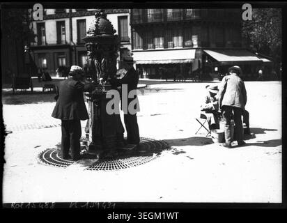 Während der Hitzewelle im Jahr 1911 trinken die Menschen Wasser an einem Wallace-Brunnen in Paris, was den Zugang der Öffentlichkeit zu Wasser und die Reaktion der Städte auf extreme Temperaturen im Paris des frühen 20. Jahrhunderts veranschaulicht. Stockfoto
