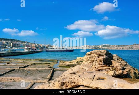 Blick auf die felsige Küste und den Pier mit Ausflugsschiffen in Bugibba. St. Paul's Bay. Malta Stockfoto