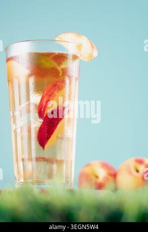 Hohes Glas kalten Pfirsicheistees mit Obstscheiben und Eiswürfeln auf einem hellen Hintergrund im Freien Stockfoto
