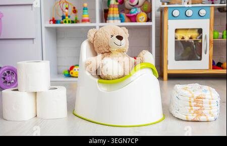 Teddybär sitzt auf einem Babytopf, Toilettentrainingskonzept im Spielzimmer. Stockfoto