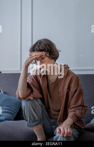 Frustriertes Teenager-Mädchen sitzt auf dem Sofa mit sorgsam nachdenklichem Ausdruck, berührt die Stirn und fühlt emotionalen Stress und mentale Erschöpfung. Angstzustände, Stockfoto