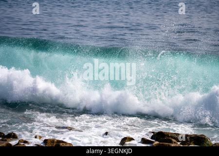 Wellen brechen an einem stürmischen Tag an einem Ufer gegen Felsen. Wasser sprüht in die Luft, während mächtige Wellen aus dem Ozean hereinströmen und eine dynamische Szene an der Küste erzeugen. Stockfoto