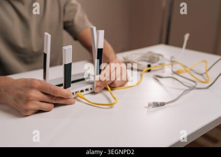 Nahaufnahme der Techniker, die ein gelbes ethernet-Kabel mit dem Anschluss eines modernen weißen Wireless-Routers mit mehreren Antennen verbinden, symbolisieren Stockfoto